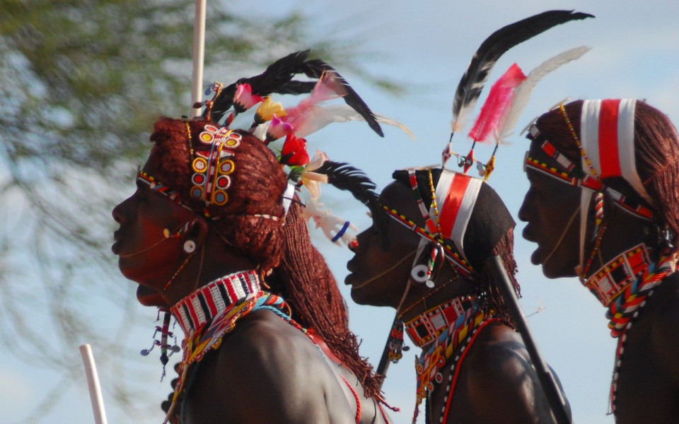 Männer in traditioneller Kleidung mit buntem Schmuck und Federn, die in einer Zeremonie in Kenia teilnehmen.