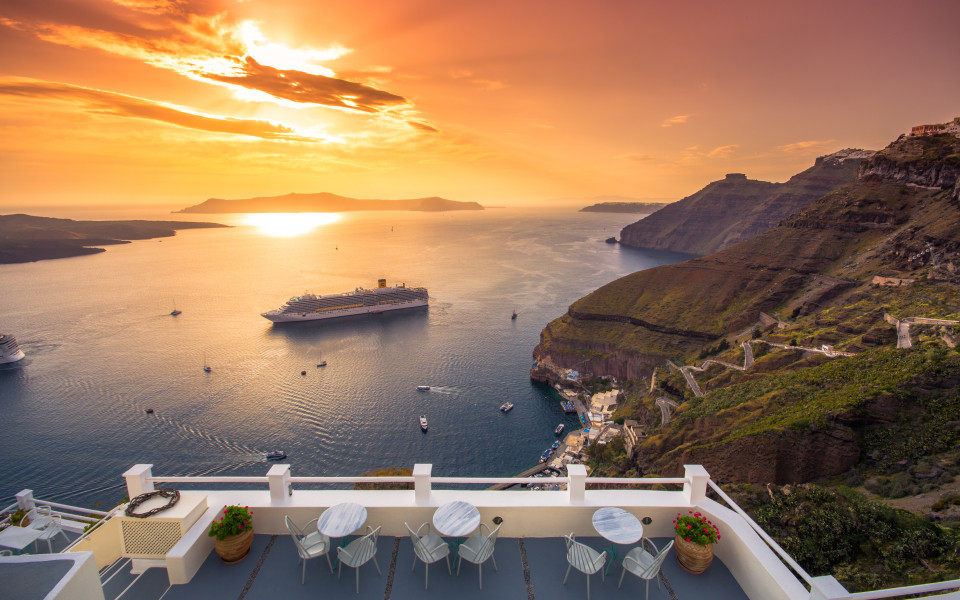 Erstaunlicher Abendblick auf Fira, Caldera, Vulkan von Santorini, Griechenland mit Kreuzfahrtschiffen bei Sonnenuntergang.